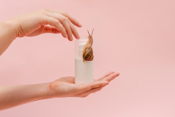 Elegant hand with cosmetic white bottle with snail. Mockup for your brand. Skin care product, spa,...