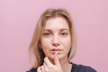 Young woman with virus herpes touching lips against pink background. Herpes blisters