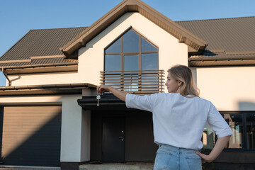 Woman holding key with new house background. Property lease real estate for relocation. Leasing insurance and purchase concept. Real estate investment concept. Buying or renting