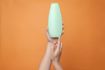 Hand holding shampoo light bottle isolated on solid orange background. Package for cosmetics product, your brand, spa, beauty. Space for text