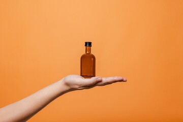 Elegant hand holding small glass blank bottle mockup on orange background. Package for cosmetics product, nutritional supplements, mixture, alcohol. Space for text