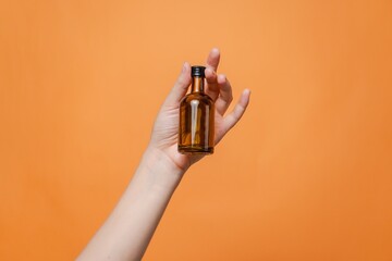 Elegant hand holding small glass blank bottle mockup on orange background. Package for cosmetics product, nutritional supplements, mixture, alcohol. Space for text