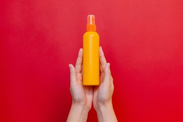 Female hand holding orange spray cosmetic bottle on the solid red background. Package, your brand