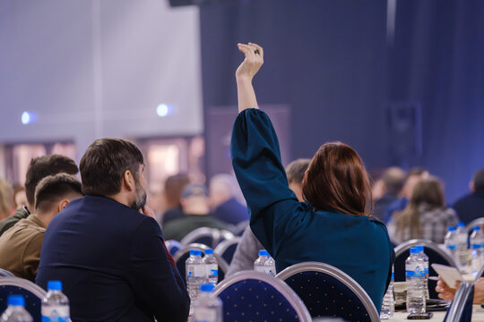 Participant raising hand during a business conference, engaging in active discussion and presentation.