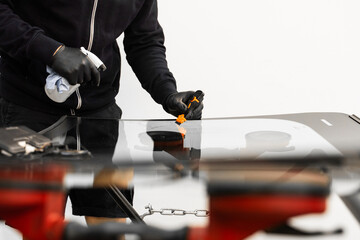 Technician uses scraper to clean the surface of a new windshield post-replacement. Technician...