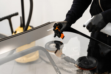 Technician uses scraper to clean the surface of a new windshield post-replacement. Technician...
