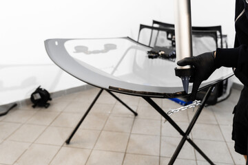 Applying adhesive to a car windshield using a caulking gun. Urethane caulking gun applies flexible adhesive, forming a watertight seal at car windshield replacement.