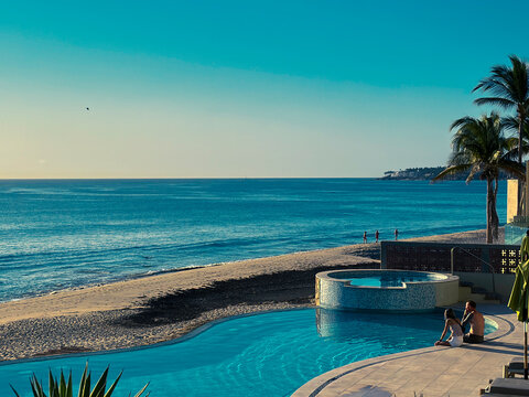 Beachfront pool with ocean view and palm trees at sunset