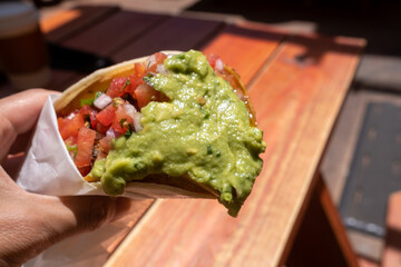 Hand holding a burrito wrapped in foil with guacamole and shredded meat visible inside in Burlingame, CA, on May 8, 2021