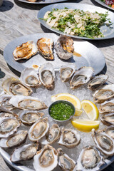 Side view of a round metal tray filled with raw oysters on the half shell, served with lemon and mignonette