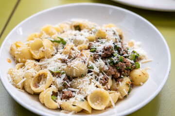 Wide plate of orecchiette pasta mixed with crumbled sausage and broccoli, topped with parmesan shavings