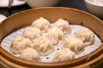 Round bamboo steamer basket filled with freshly made xiao long bao soup dumplings on a dining table
