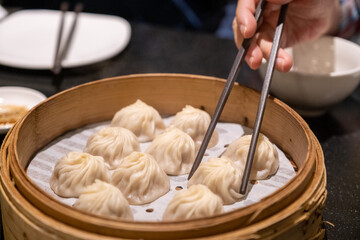 A pair of chopsticks lifts one xiao long bao from a bamboo steamer full of freshly steamed soup dumplings