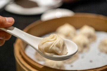 A juicy soup dumpling sits atop a white spoon above a full bamboo steamer filled with xiao long bao, San Francisco, CA, May 30, 2021