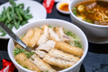 Bowl of sesame noodles garnished with green onions and sesame seeds, served with side dishes and condiments