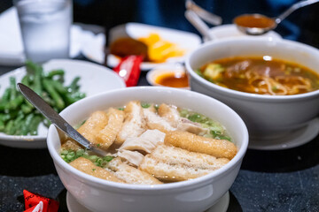Chopsticks pull up a portion of sesame noodles from a deep white bowl, surrounded by other savory side dishes