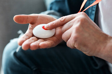 Closeup of man's hand pressing alarm button for emergency on his chest, home interior....