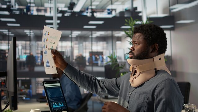 African american CEO wears a medical foam collar to protect his neck injury, dealing with a discomfort and struggling to solve operations. Entrepreneur working hard to achieve growth. Camera B.