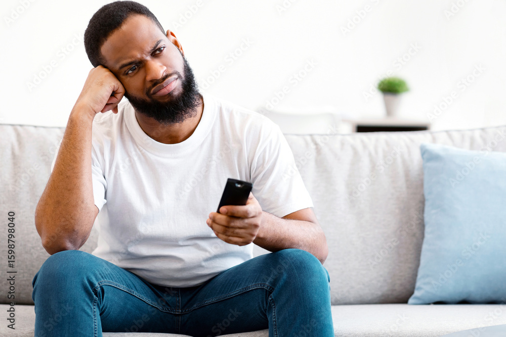 Poster boring television program. bored african american guy watching tv switching channels with remote con