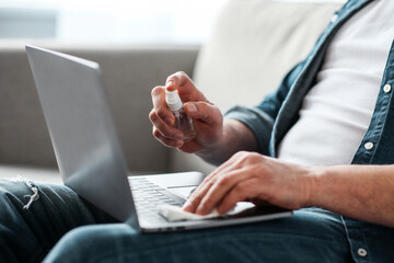 Unrecognizable man disinfecting gadgets, cropped. Male hands using disinfectant mist spray and...