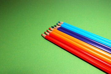 Diagonal set of sharpened red, orange, purple, and blue color pencils on smooth green background...