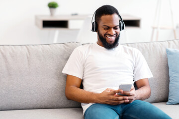 Happy African Man Listening To Music Using Mobile Phone And Wearing Wireless Earphones Sitting On...