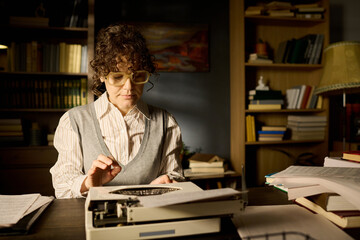 Middle aged Caucasian woman typing on vintage typewriter in office surrounded by stacks of...