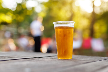 Plastic cup of cold beer on outdoor wooden table