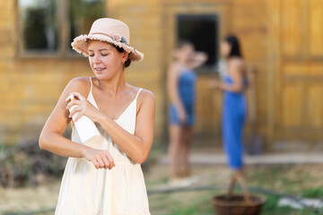 Young woman in dress applying sunscreen outside country house