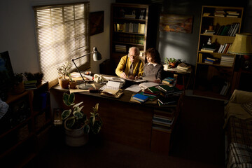 Senior Caucasian man and young adult Caucasian woman sitting at desk working together with...