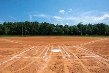 Baseball field under a clear blue sky in a rural setting during daytime with lush green trees in...