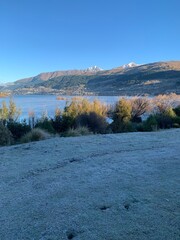 White grass covered in frost with lakeside scenic view and snow-covered mountains, sunny distance