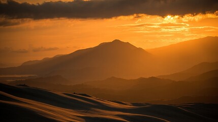 Golden sunrise over a mountain range, silhouetted against a dramatic orange-yellow sky, with vast white sand dunes at the foreground