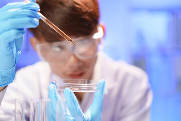 Female lab technician holding pipette above Petri dish. Young scientist doing analysis in the...