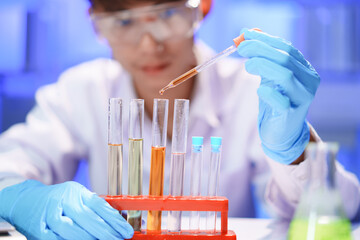 Scientists working in Laboratory using pipette dropping liquid sample into test tube.