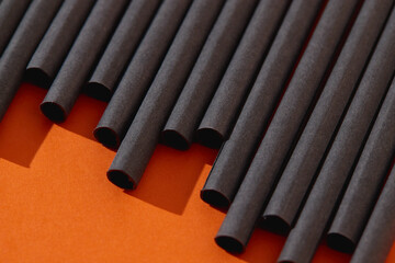 Black paper straws on orange background. Halloween party