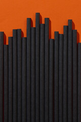 Black paper straws on orange background. Halloween party