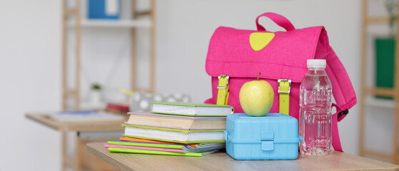 Apple with lunchbox, books and backpack on desk in classroom