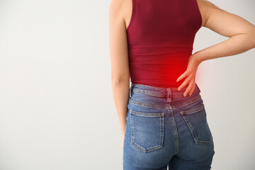 Young woman suffering from back pain on light background