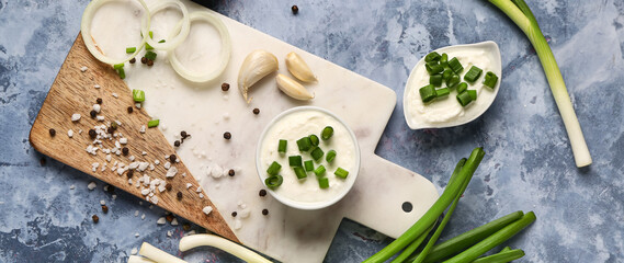 Bowl and gravy boat of tasty sour cream with sliced green onion on blue background