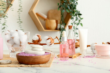 Set of cosmetic products, bath supplies and cotton branch on light table in room