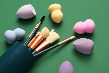 Makeup sponges and brushes on green background