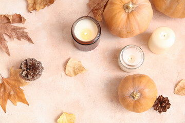 Burning candles with pumpkins, autumn leaves and pine cones on beige background