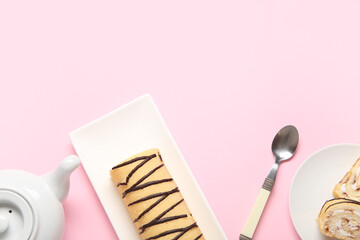 Plates with sweet sponge cake roll and tea pot on pink background