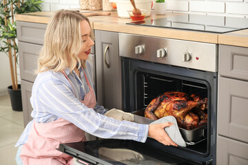 Beautiful young woman taking tasty baked turkey from oven in kitchen. Thanksgiving Day celebration