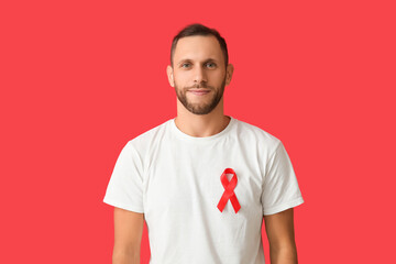 Young man with red ribbon on color background. AID awareness concept