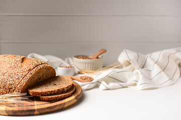 Wooden board with sliced loaf of bread and wheat spikelets on white table