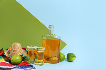 Bottle of tequila with shots and lime on color background