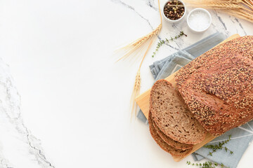 Wooden board with sliced loaf of bread, wheat spikelets and thyme on white grunge background