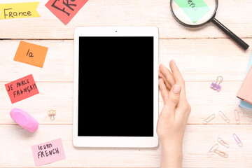 Female hand with modern tablet computer and French words on white wooden background, closeup